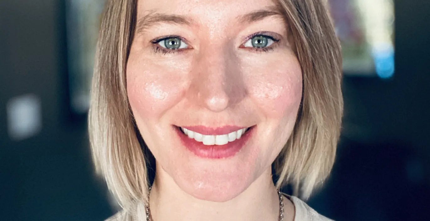 Jaclyn a des cheveux blonds et courts et porte un haut décontracté – elle est photographiée à l’extérieur.