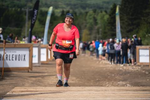 Andrea, wearing a red t-shirt and black shorts crosses the finish line and smiles proudly.