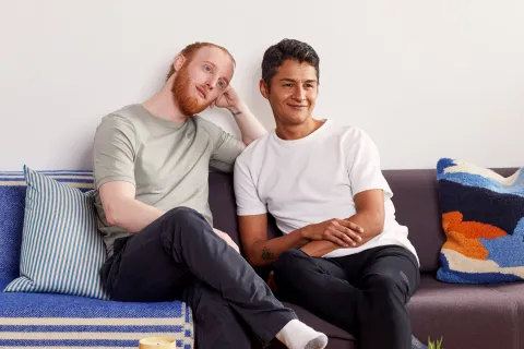 Marc, in a light green t-shirt and dark pants, sitting on a couch next to Richard, who is wearing a white t-shirt and dark pants.
