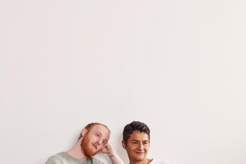 Marc, in a light green t-shirt and dark pants, sitting on a couch next to Richard, who is wearing a white t-shirt and dark pants.