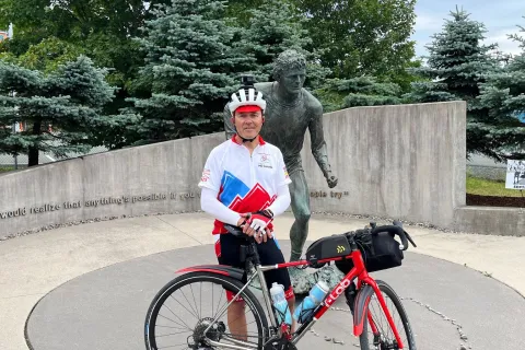 Marcel standing with his bike in front of a Terry Fox monument in St. John's, Newfoundland.