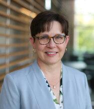 An image of Dr. Marcia Finlayson, an MS researcher. She has short hair and is wearing tortoiseshell glasses, earrings, a patterned shirt and a blazer.