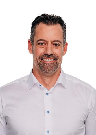 A smiling man with short dark hair and a trimmed beard, wearing a white button-up shirt.