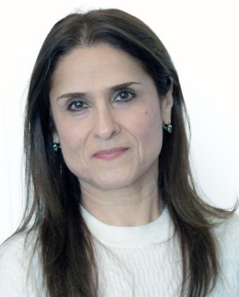 A woman with long brown hair is wearing small hoop earrings and a white sweater.