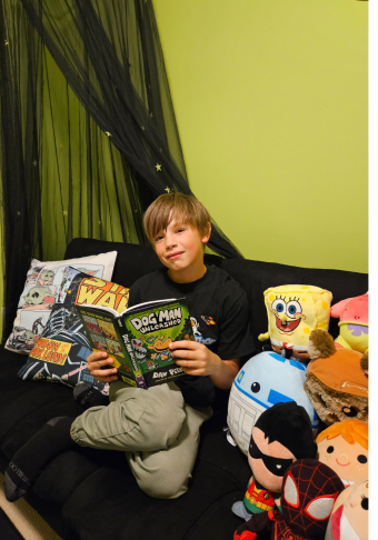 Sawyer, sitting on a couch, wearing a black shirt and green pants, holding a book.