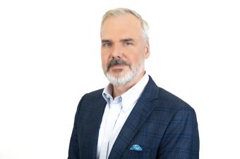 A man with short salt and pepper hair and beard is wearing a navy suit.