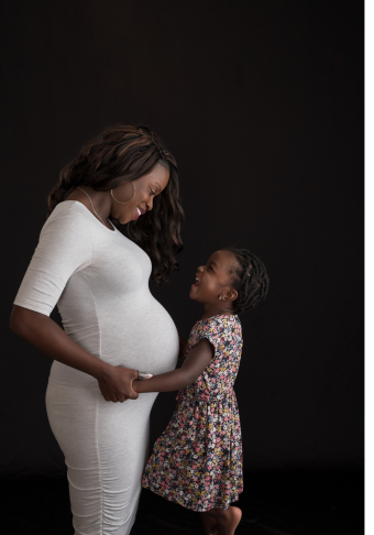 Janelle, wearing a white dress, holding hands with her daughter, wearing a pink floral dress.