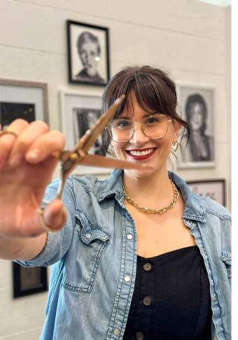 Jess, wearing a black top and blue jacket, holding scissors.