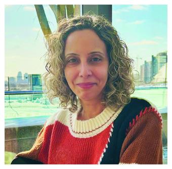 A woman with medium length curly blond hair sit in front of a skyline.