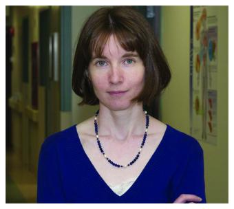 A woman with chin length auburn hair is wearing a blue shirt and a complimenting necklace.