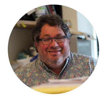 Smiling middle-aged man with glasses and a floral shirt in a circular cropped photo.