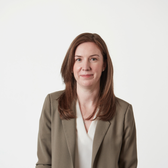 Professional headshot of a smiling woman with brown hair wearing a beige blazer.