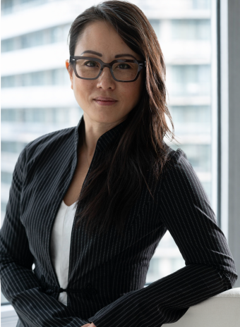 Professional woman in black pinstripe blazer and glasses, posing confidently in an office setting.