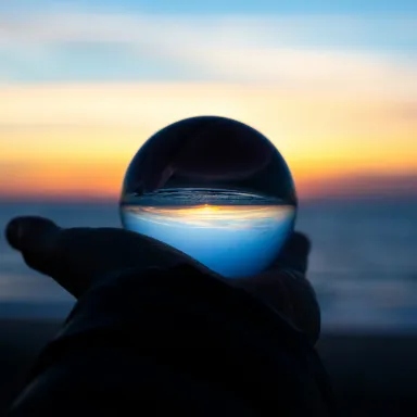 Hand holding a crystal ball reflecting a vivid sunset over the ocean.