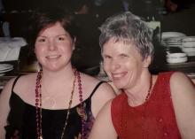 Two smiling women wearing beaded necklaces at an indoor event.