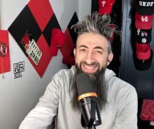 Smiling man with a beard speaking into a microphone in a red and black decorated room.