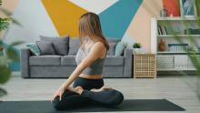 Woman practicing yoga in a seated twist pose on a mat in a colorful modern living room.