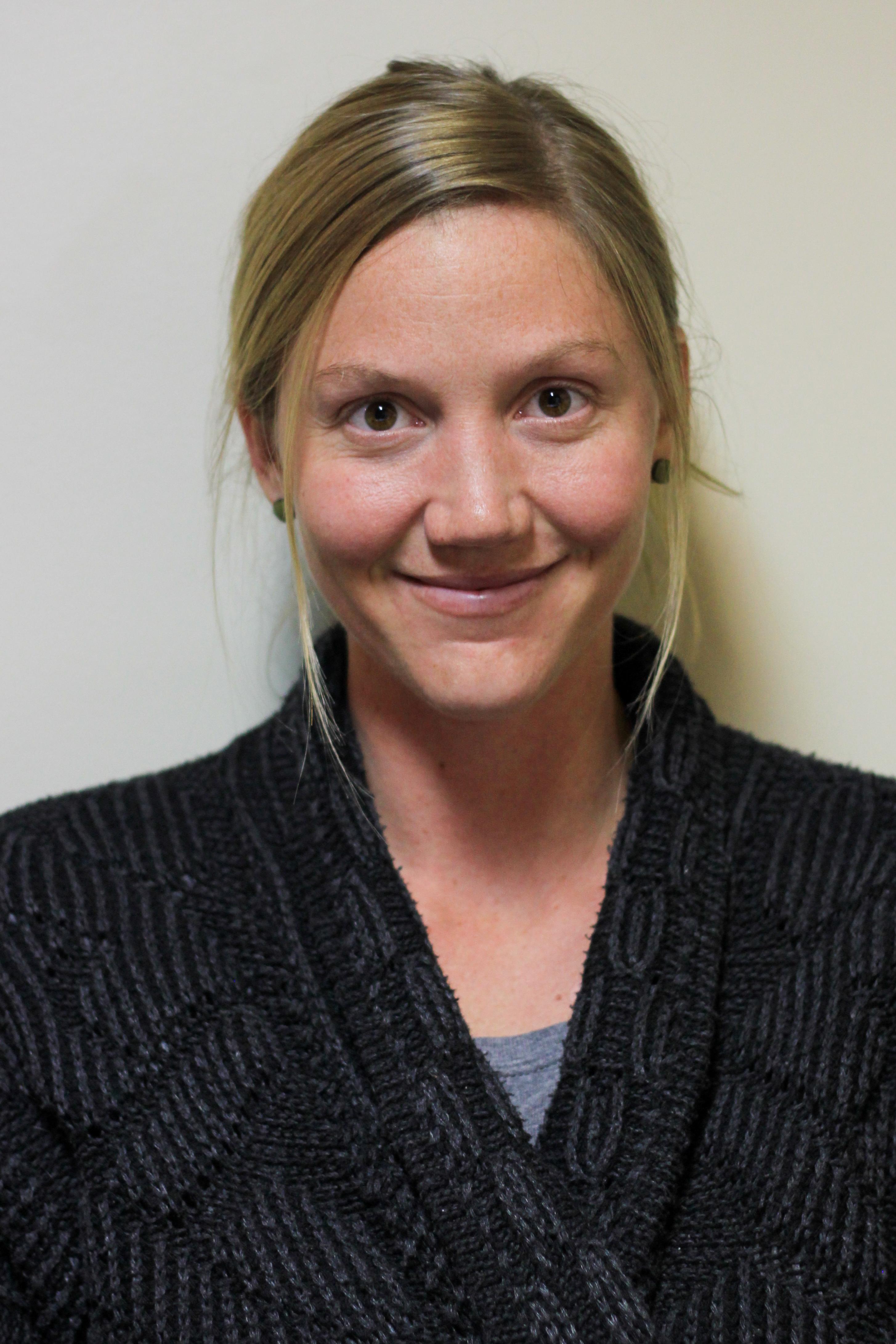 A blonde woman with hair tucked behind her ears smiling warmly.