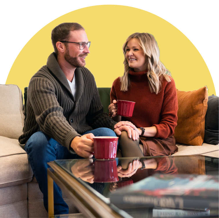 A man and a woman sit on a cozy couch facing each other having coffee.