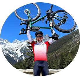 A man fully dressed in biking gear holds his bike upside down above his head