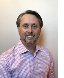 [Geoff Robinson, male wearing a pink checkered shirt, smiling against tan background]