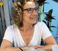 [Heather Blumenthal, a wavy-haired brunette female wearing a white shirt while sitting at a table]