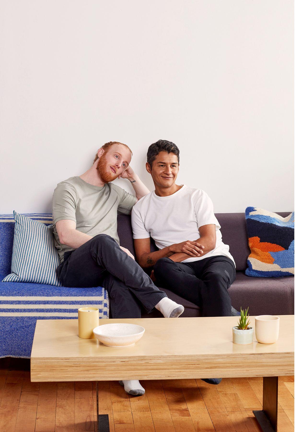 Marc, in a light green t-shirt and dark pants, sitting on a couch next to Richard, who is wearing a white t-shirt and dark pants.