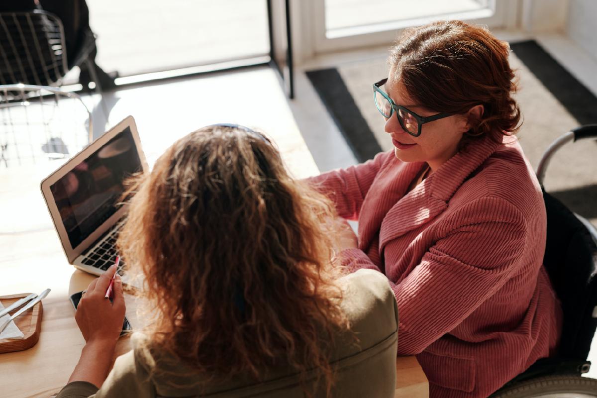 Two women at a desk looking at a computer together.