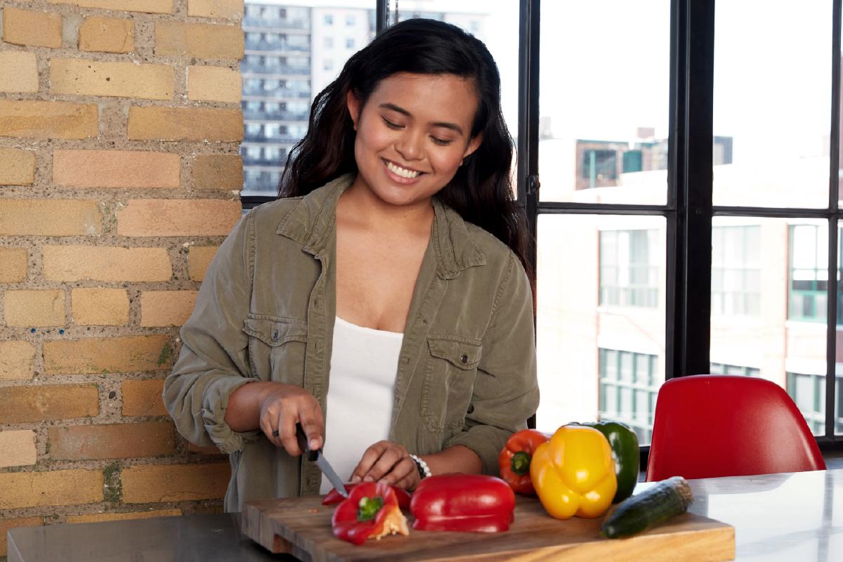 A woman cuts red peppers on a cutting board at a counter.