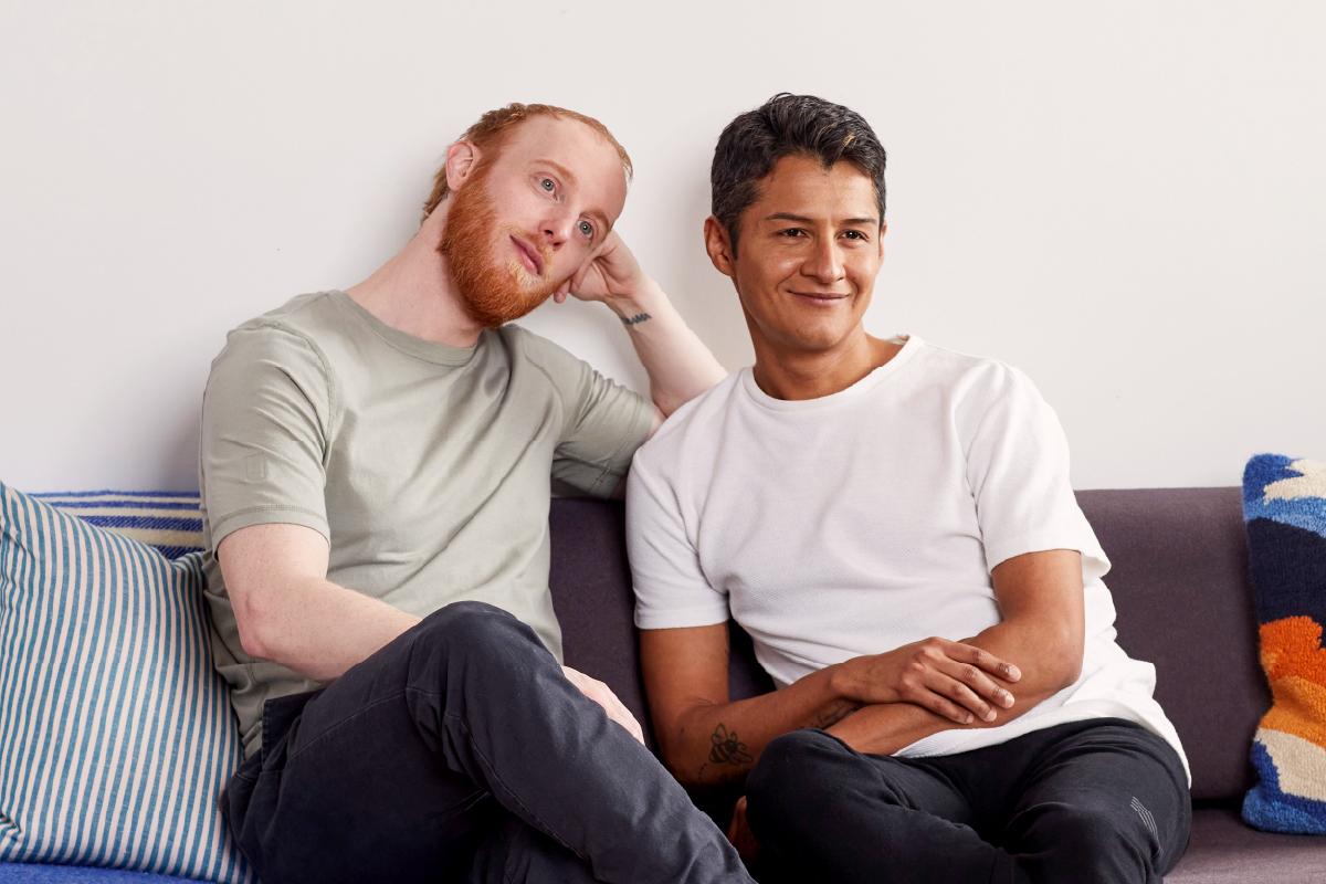 Two men sitting on a couch together watching something out of the frame.