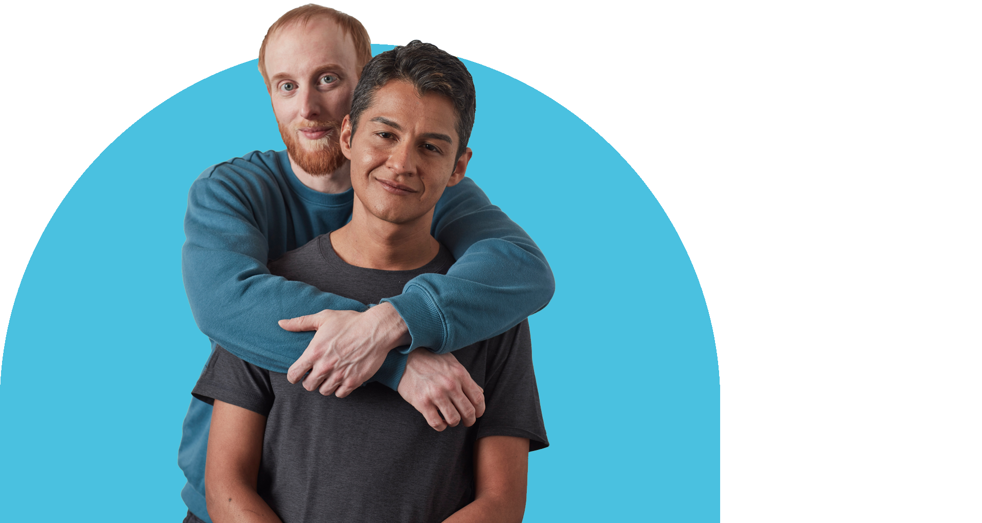Two men, one with red hair and one with dark hair, embrace and smile.