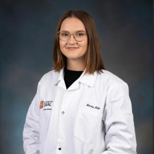 Portrait de Alexia Falle portant une blouse de laboratoire blanche avec le logo de l’Université Laval et son nom brodé, posant devant un fond professionnel.