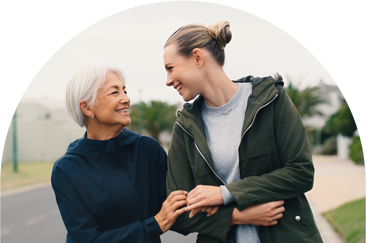 Two women look at eachother. Their arms are interlocked. One is wearing a navy hoodies and the other has a army green jacket.