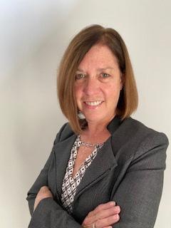 A woman with a carmel coloured bob is wearing a dark grey suit with her arms crossed and is smiling.
