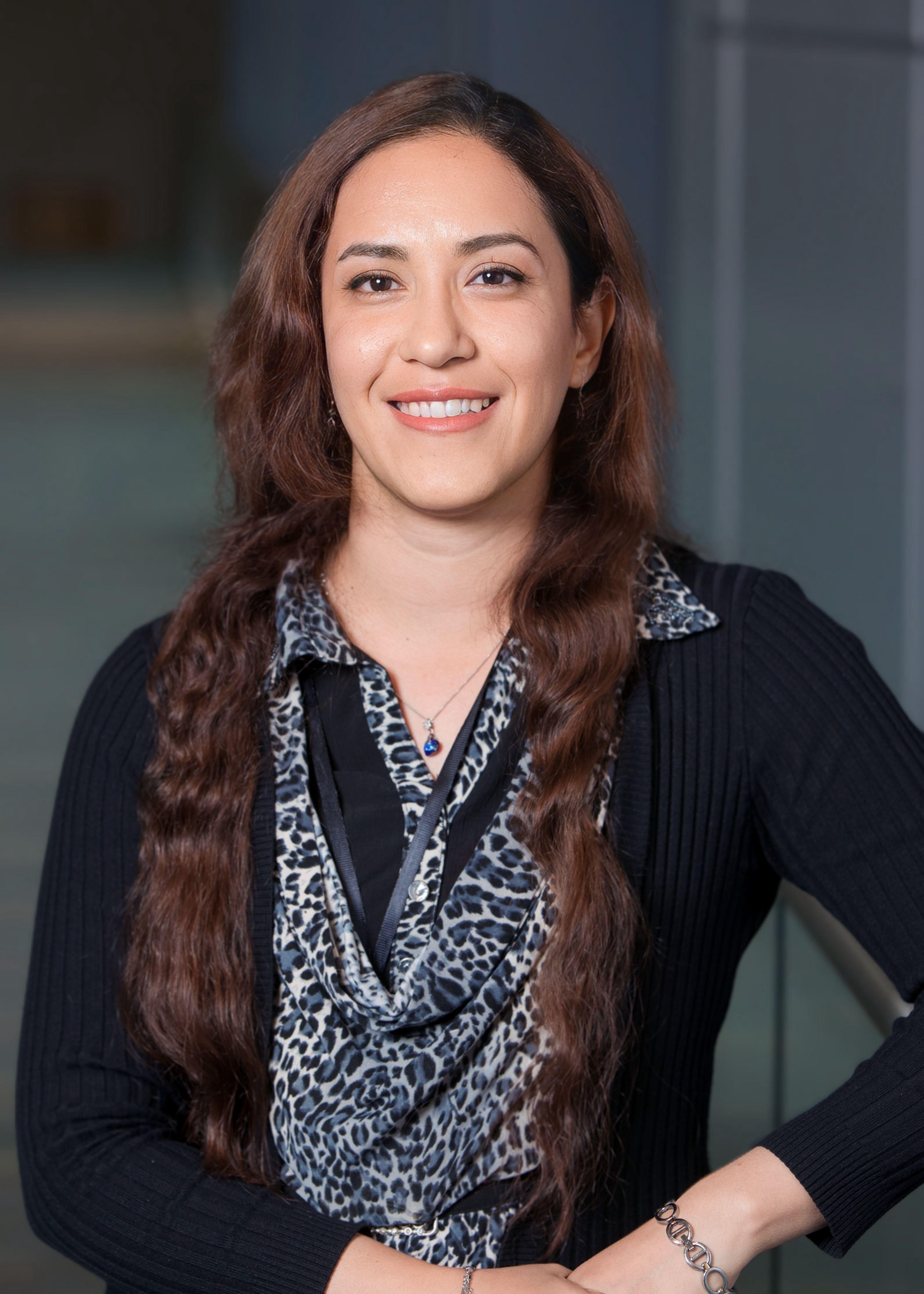 Dr. Rayatpour, wearing a black top, with long brown hair.