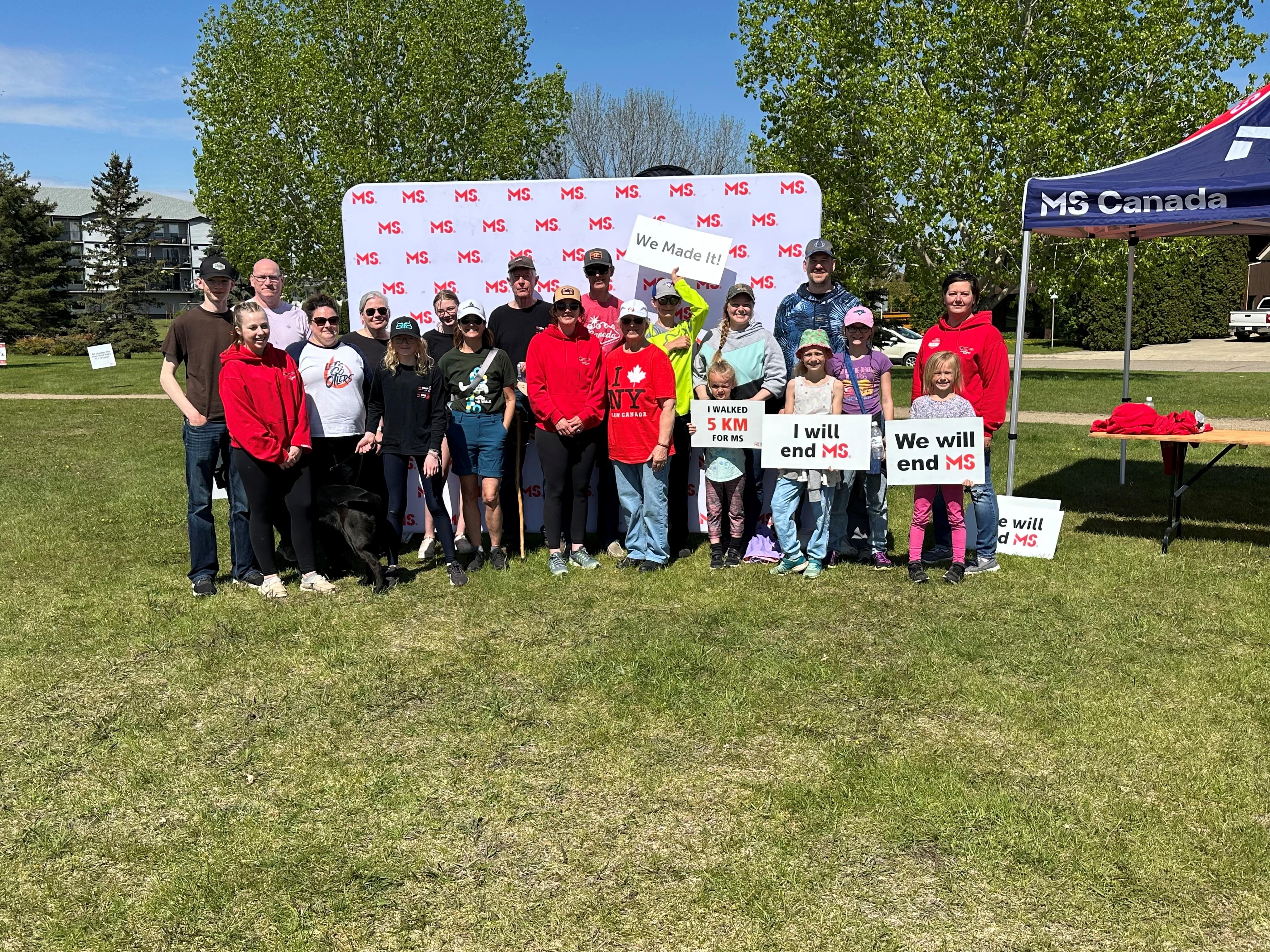 James with his MS Walk team holding signs, standing in front of the MS Canada backdrop.
