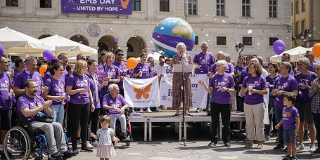 Group of people in purple shirts at an outdoor event, some in wheelchairs, holding a banner and globe balloon.