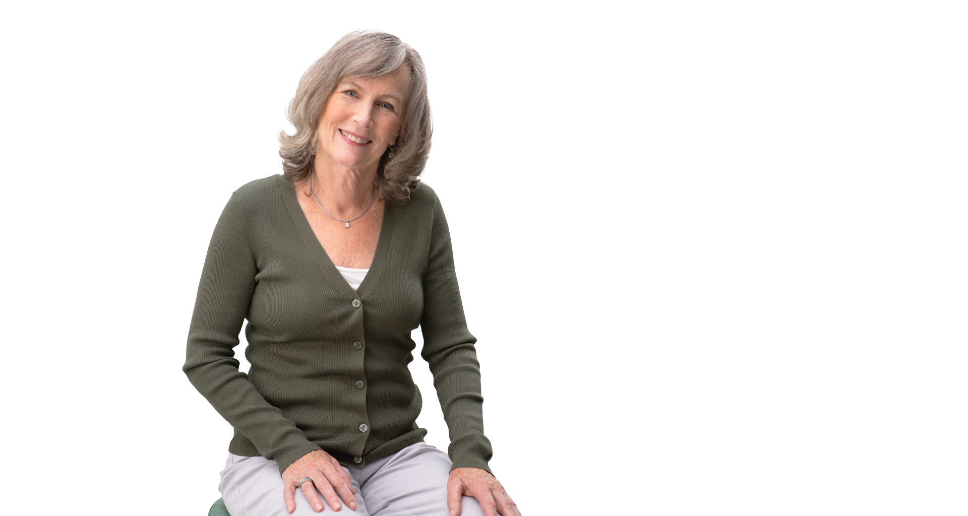 Smiling middle-aged woman with gray hair wearing a green cardigan, seated against a white background.