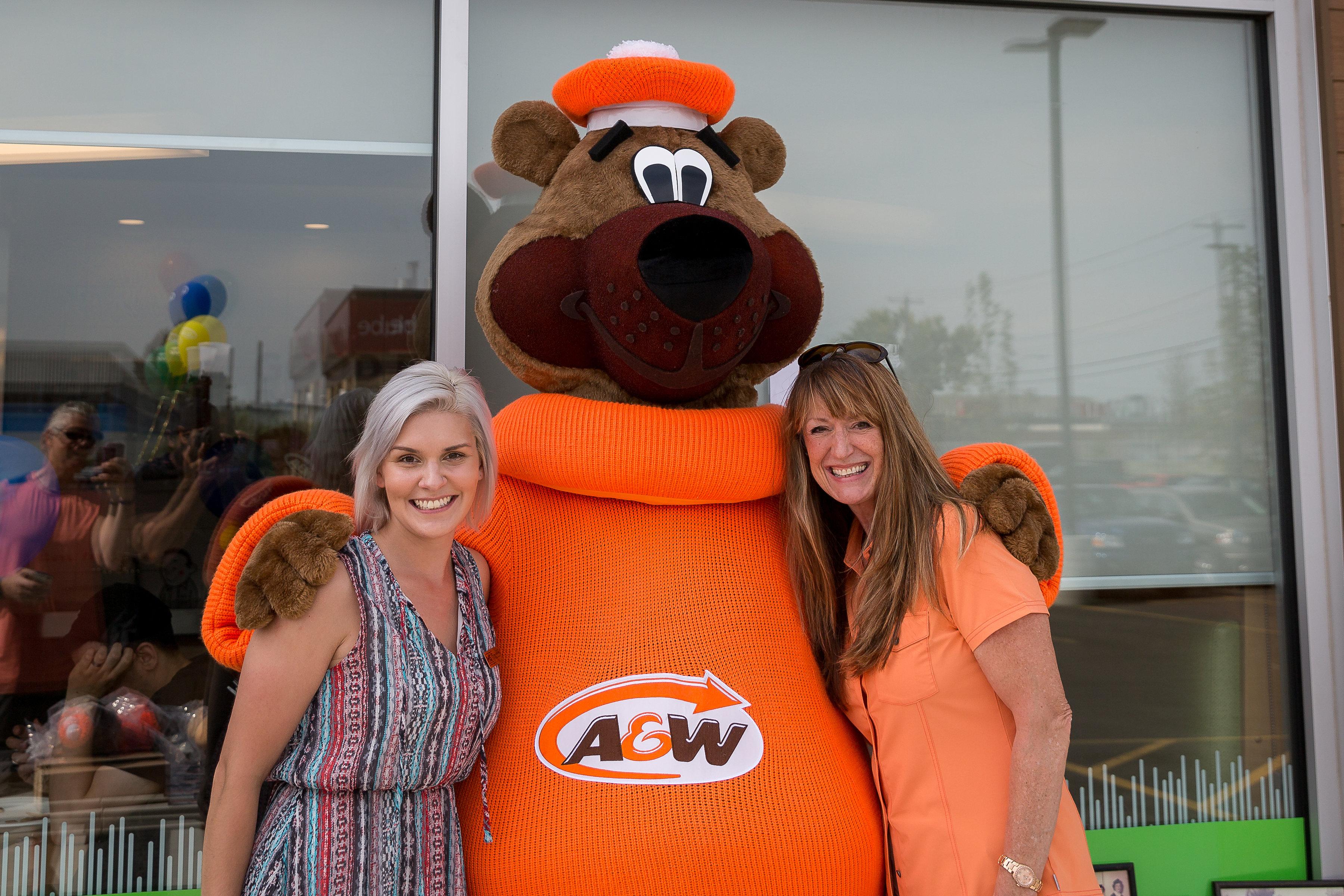 Two women posing with the A&amp;W root beer bear mascot outdoors at a restaurant.