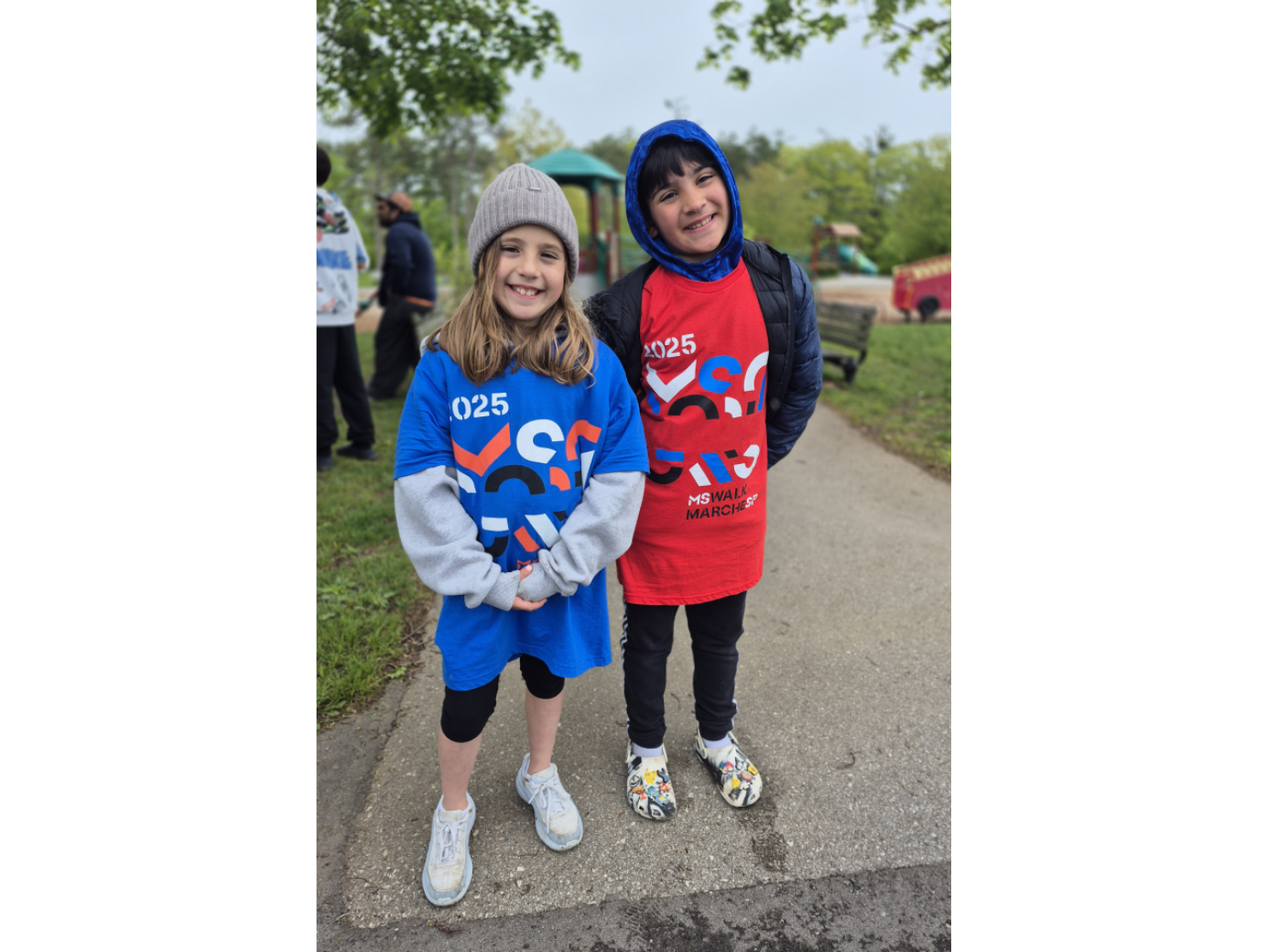 Frankie (à droite) et son amie Sophia (à gauche) sont dans un parc et ils sourient. Chacun d’eux porte un t-shirt de la Marche SP. 