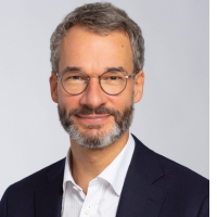 Professional headshot of a middle-aged man with glasses and a beard, wearing a dark blazer.