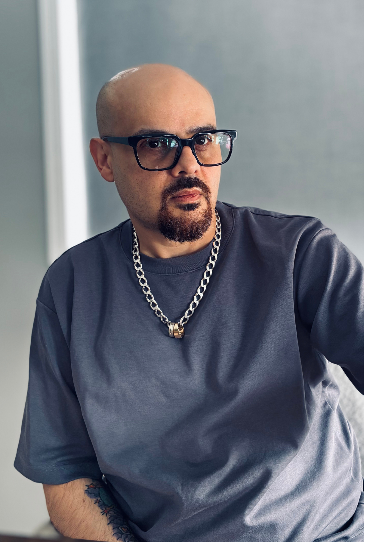 Miguel porte des lunettes, un collier à chaîne argentée et un t-shirt gris.