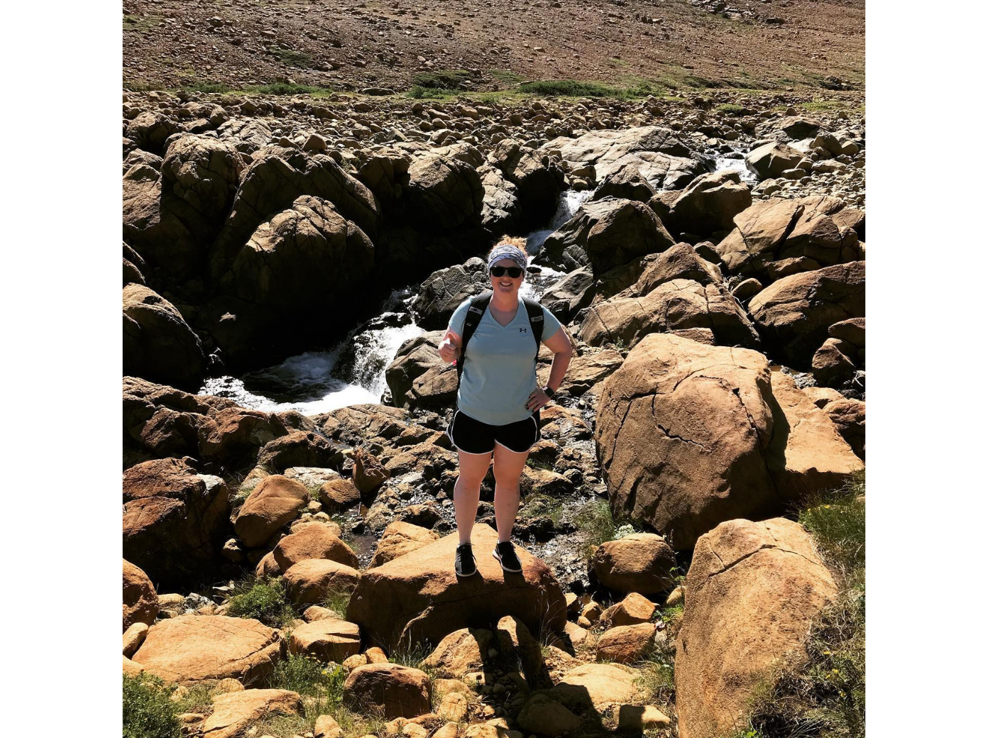 Janice se trouve parmi des rochers de grande taille, près d’un torrent, sous un ciel ensoleillé.
