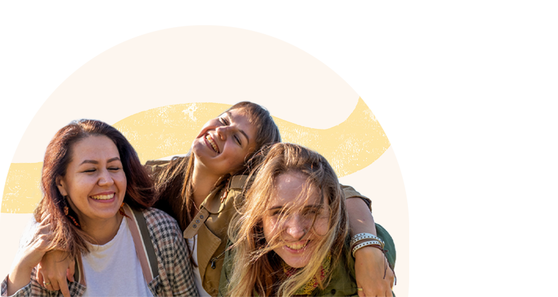 Three young women smiling and laughing together outdoors on a sunny day.