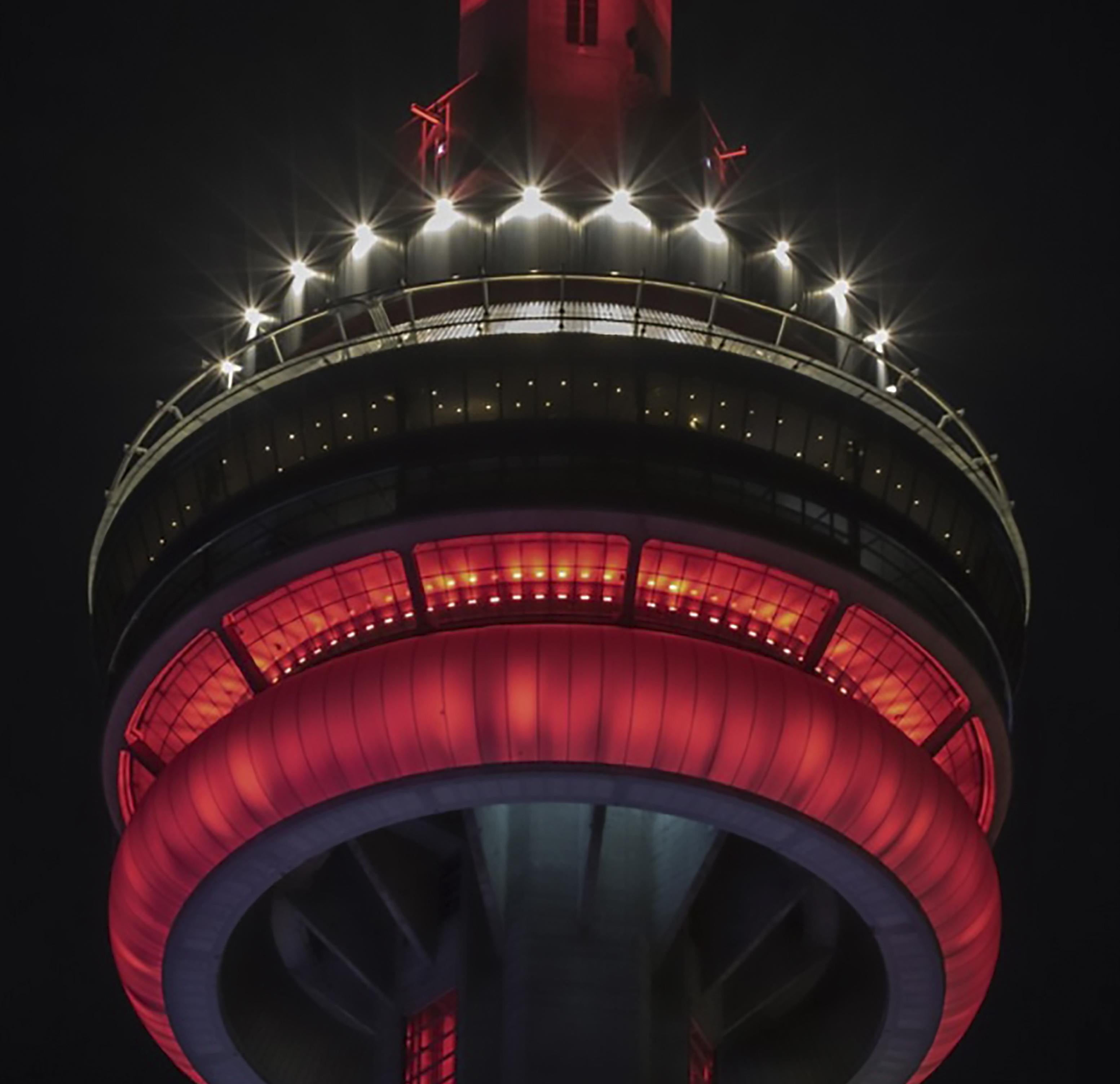 CN Tower observation deck illuminated in red lights against a dark night sky.