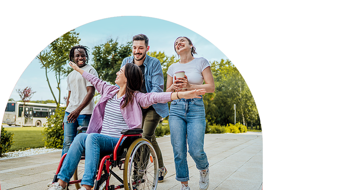 Four smiling friends outdoors, one in a wheelchair, enjoying a sunny day together.