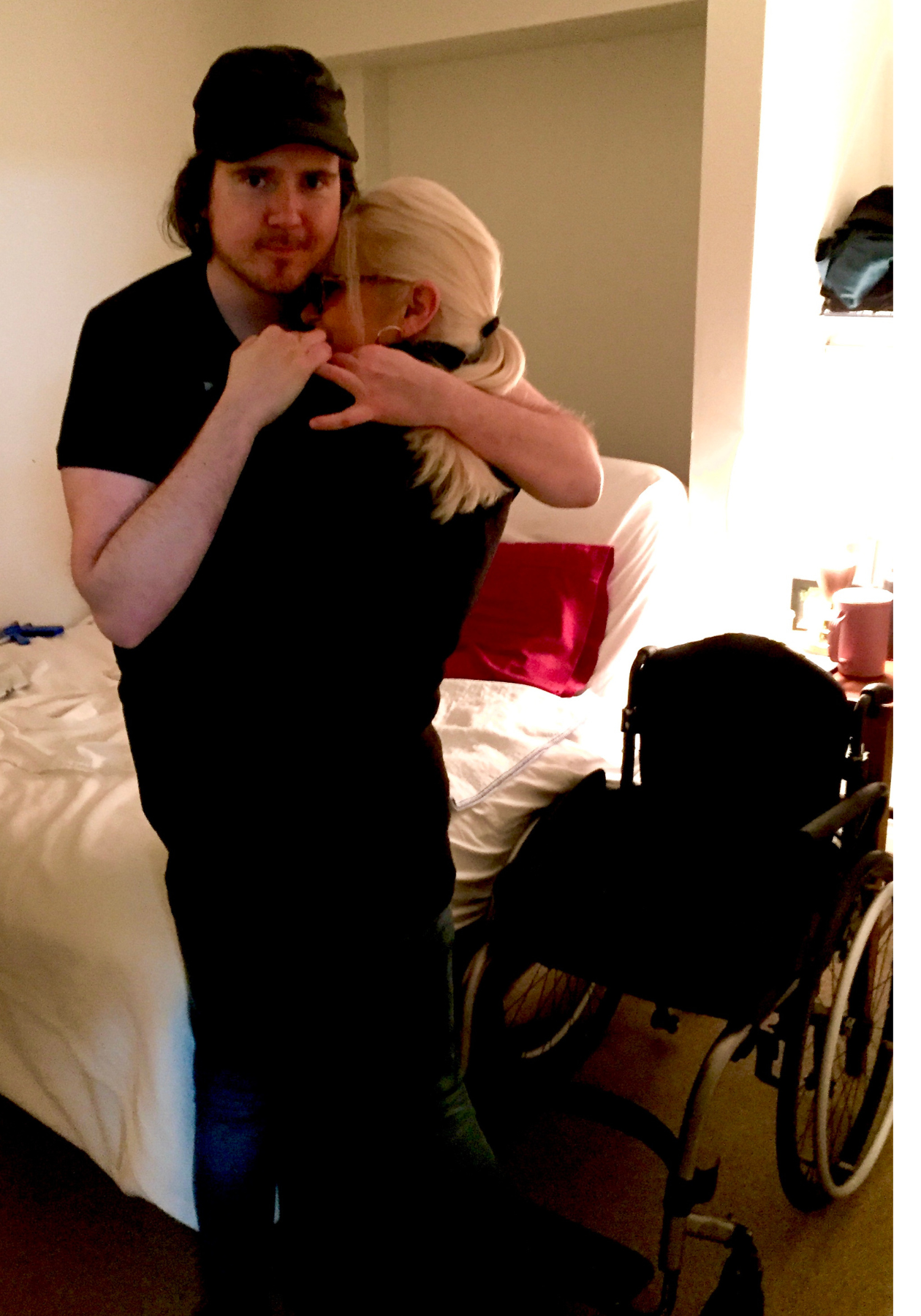 Jason et sa mère sont debout dans une chambre à coucher. Ils s’enlacent. En arrière-plan apparaissent un lit et un fauteuil roulant. 