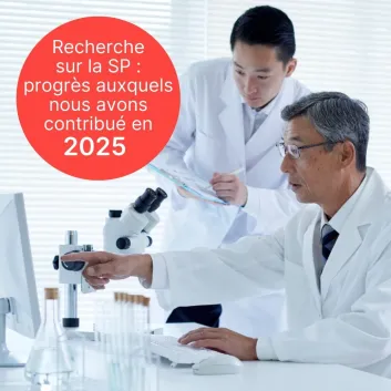 Deux chercheurs sont vêtus d’un sarrau blanc. L’un d’eux porte des lunettes et pointe du doigt un écran d’ordinateur, et l’autre tient dans ses mains une planchette à pince et un stylo. 