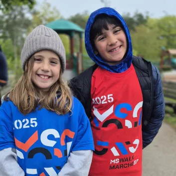 Two smiling children wearing numbered race bibs outdoors at a park event.