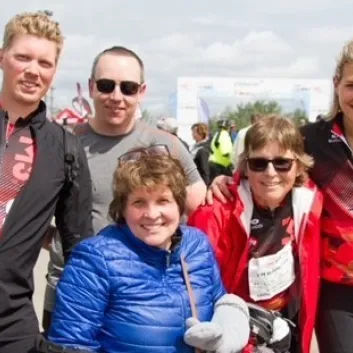 Alli et sa famille sont à l’extérieur lors d’un événement du Vélo SP et sourient devant l’objectif. Certaines personnes portent un maillot du Vélo SP. 